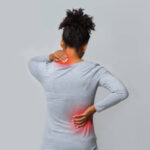 Back view of african woman rubbing her inflamed neck and loins, grey background